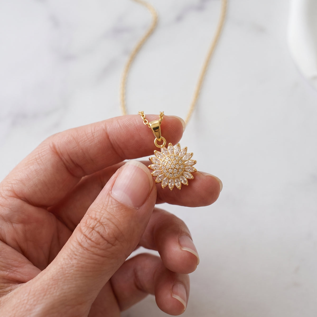Gold sunflower pendant held between the fingers to spin it