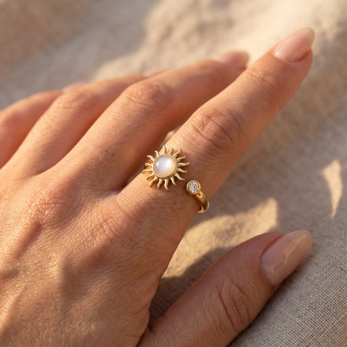 Hand on beige linen wearing the gold sun spinner ring in warm sunlight