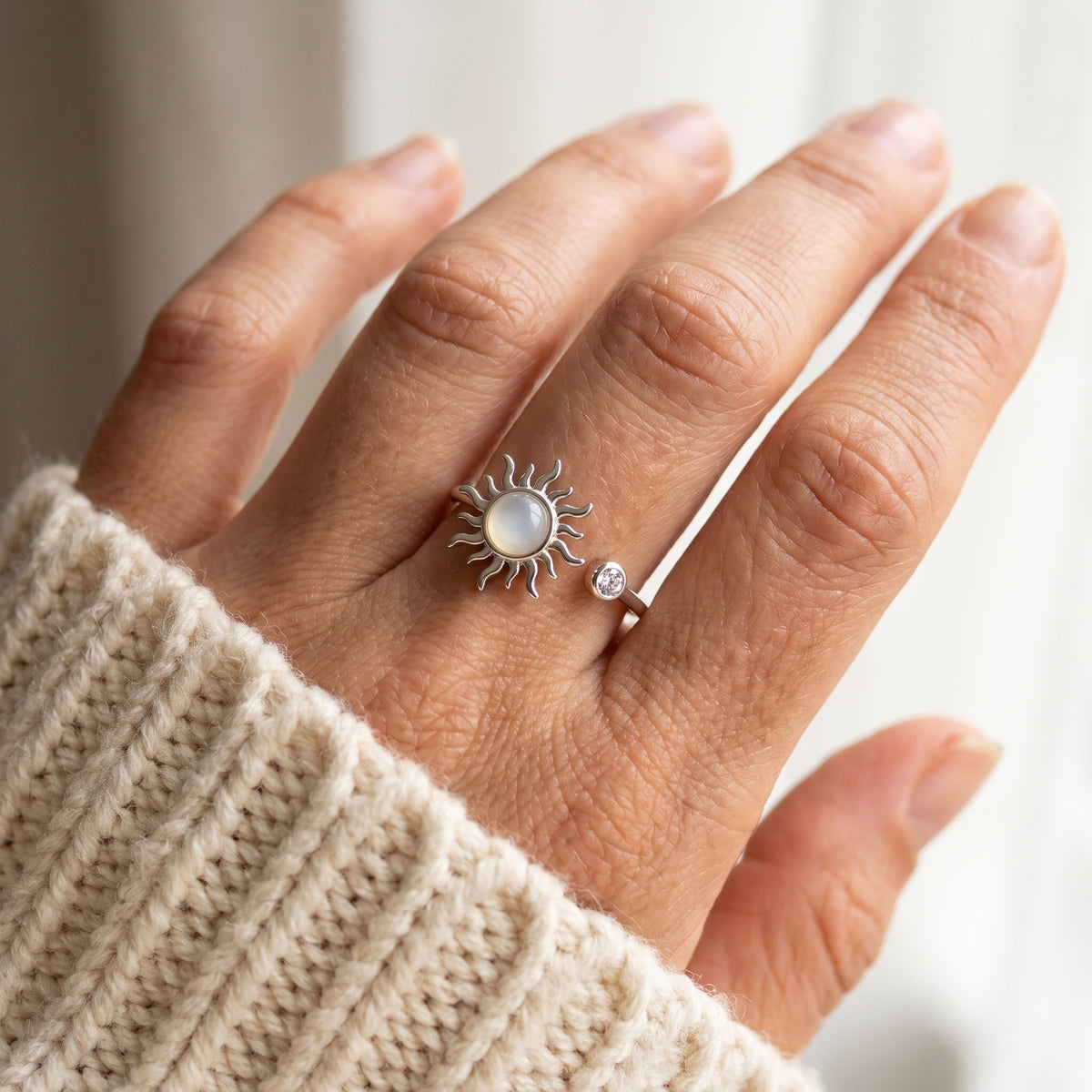 Hand at a cream knit sleeve wearing the silver sun spinner ring