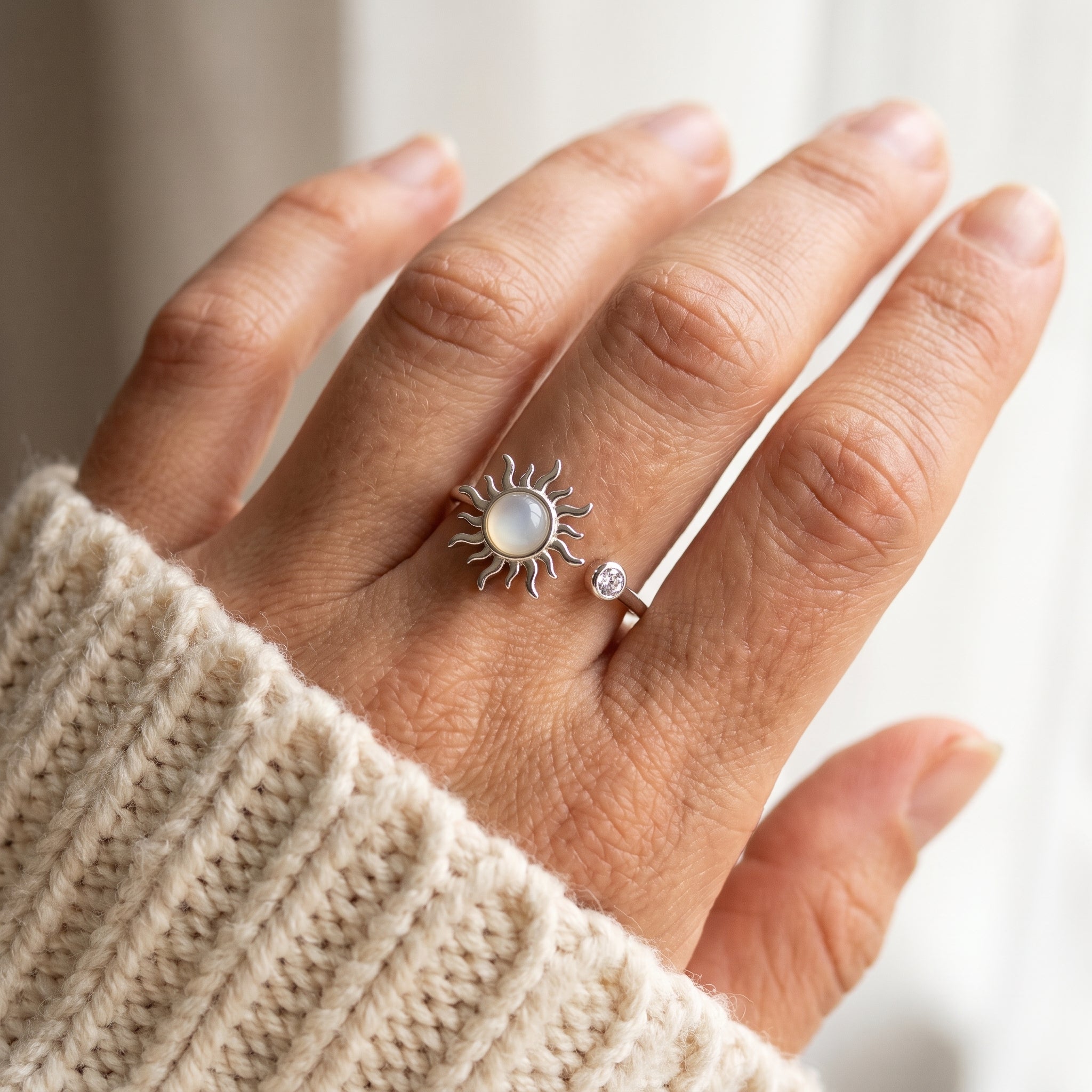 Hand at a cream knit sleeve wearing the silver sun spinner ring