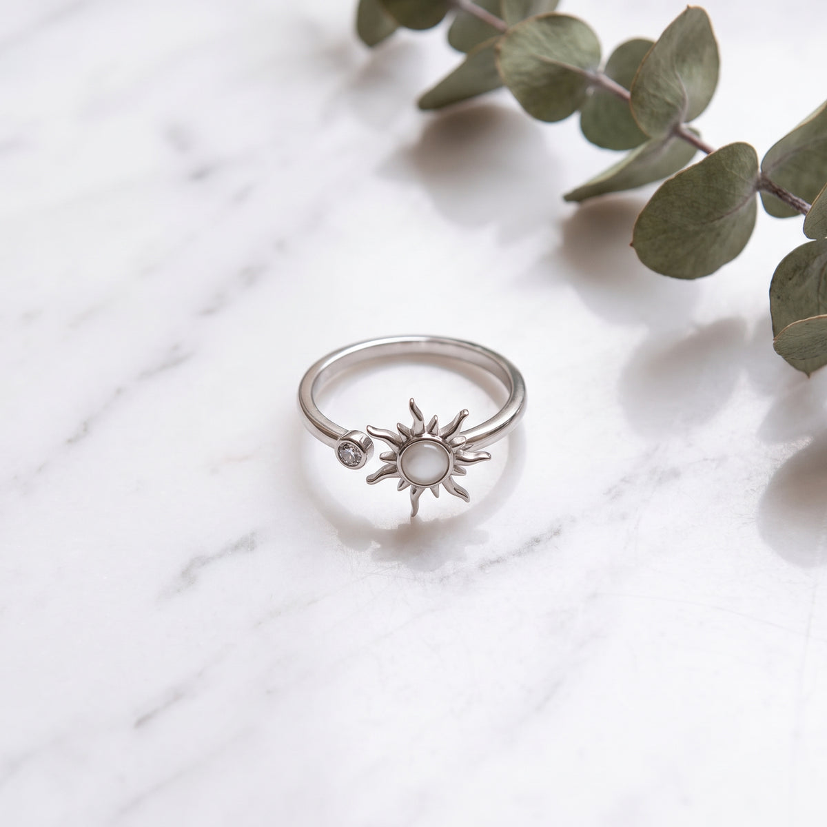 Silver sun spinner ring on white marble with eucalyptus