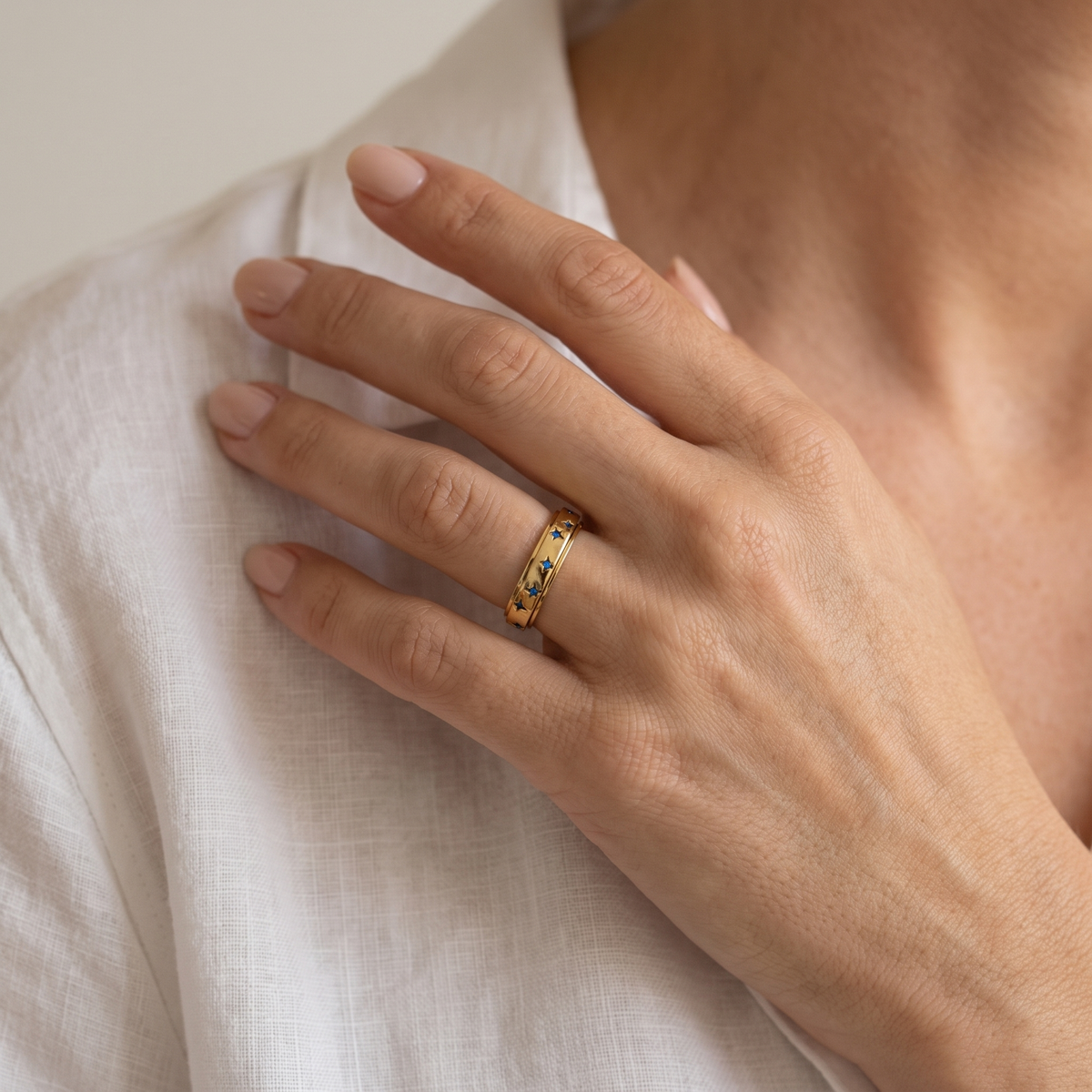 Hand at the collarbone wearing the Gold Blue Star Spinning Ring