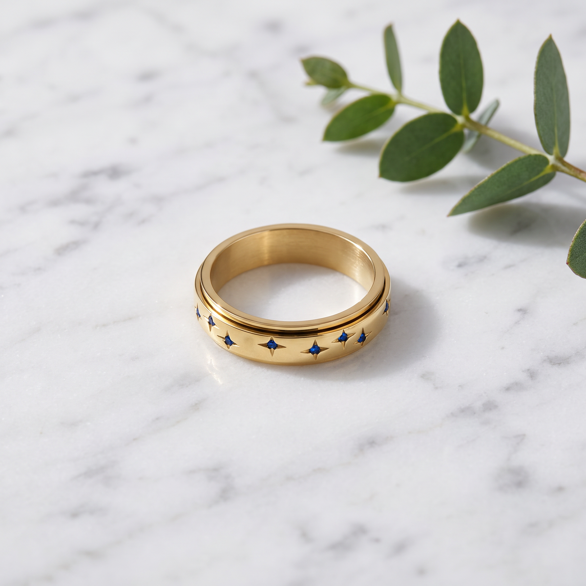 Gold Blue Star Spinning Ring on white marble with eucalyptus