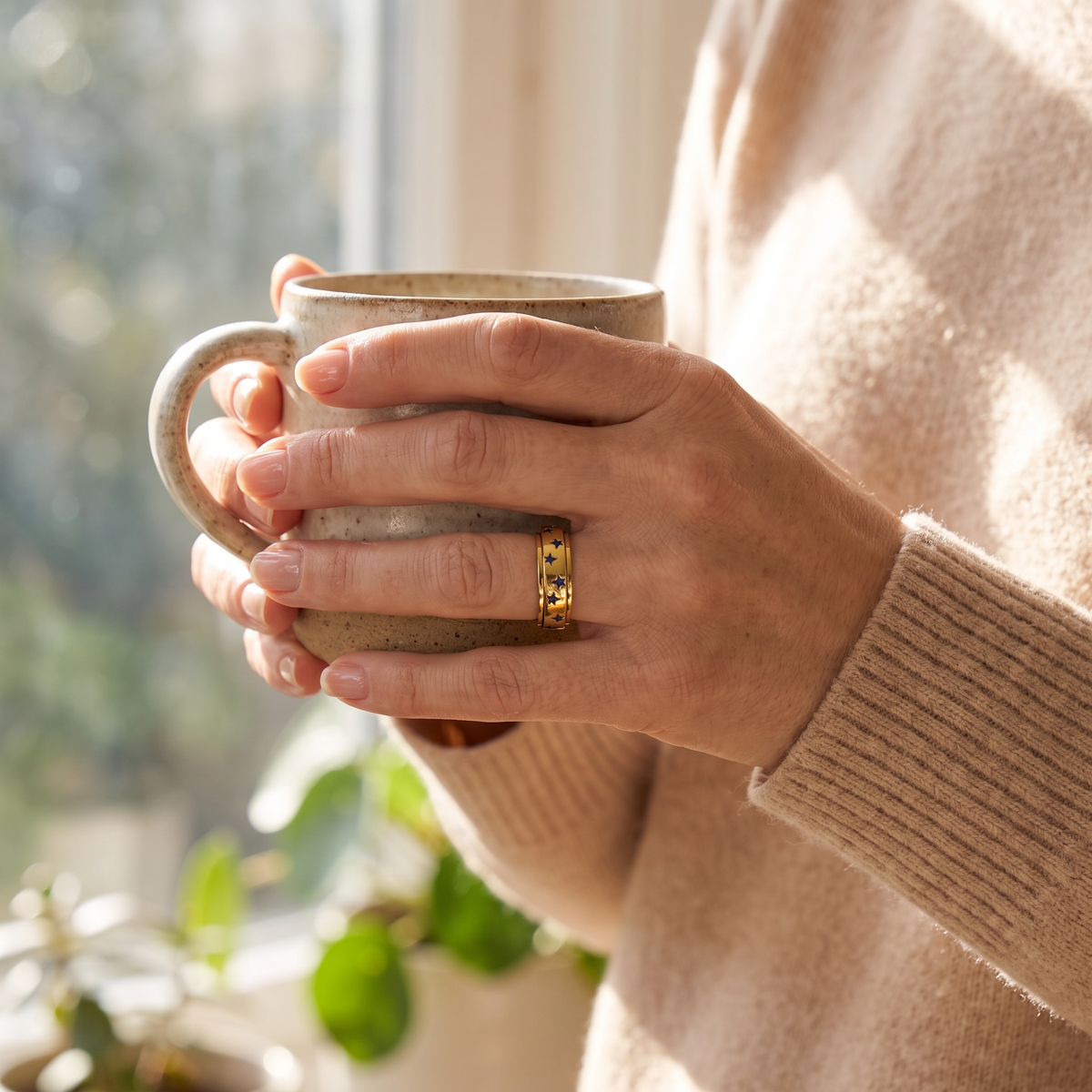 Hands holding a coffee mug, wearing the Gold Blue Star Spinning Ring