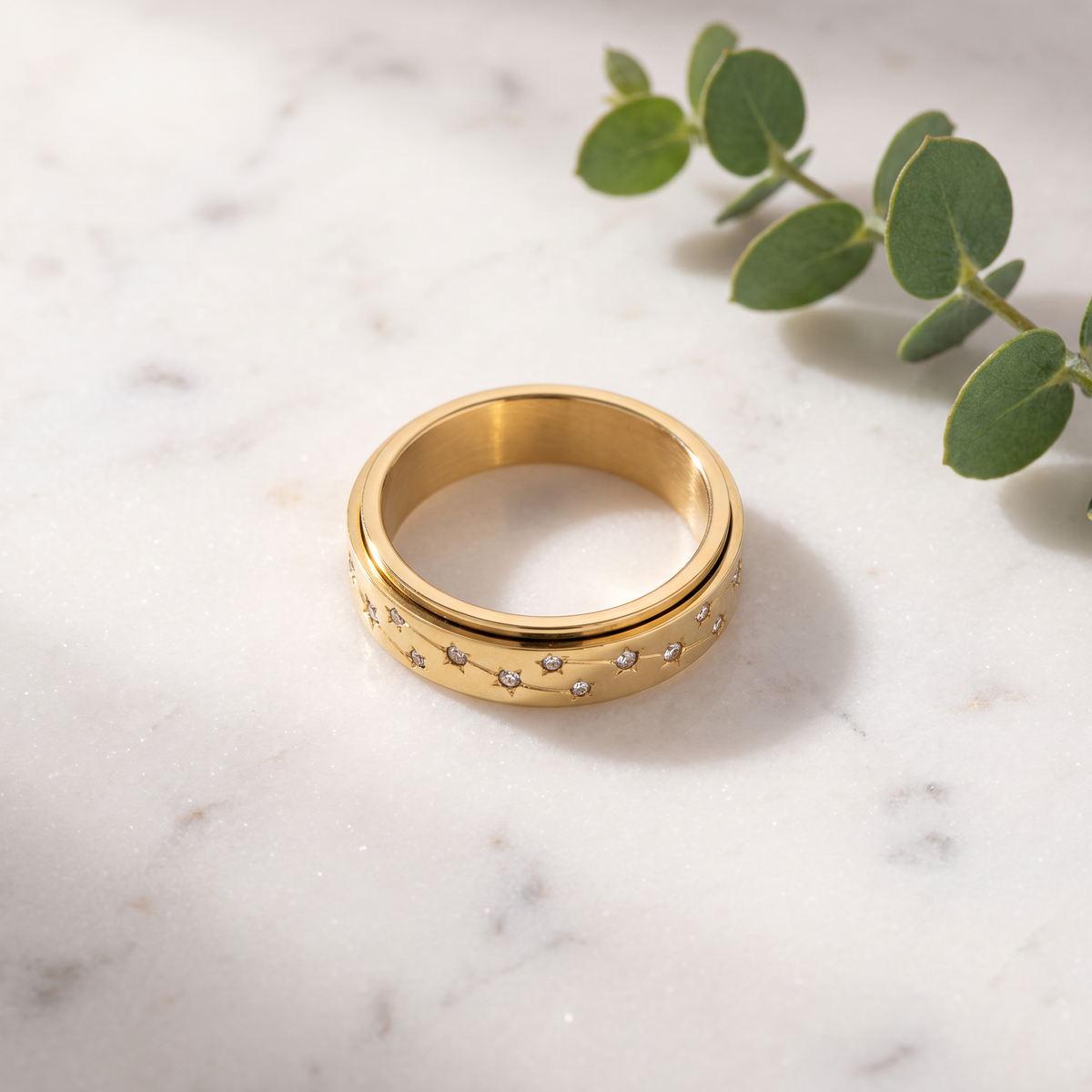 Gold Constellation Spinning Ring on white marble with eucalyptus