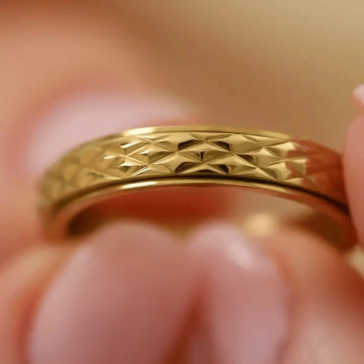 Fingers turning the gold cross-pattern spinning ring