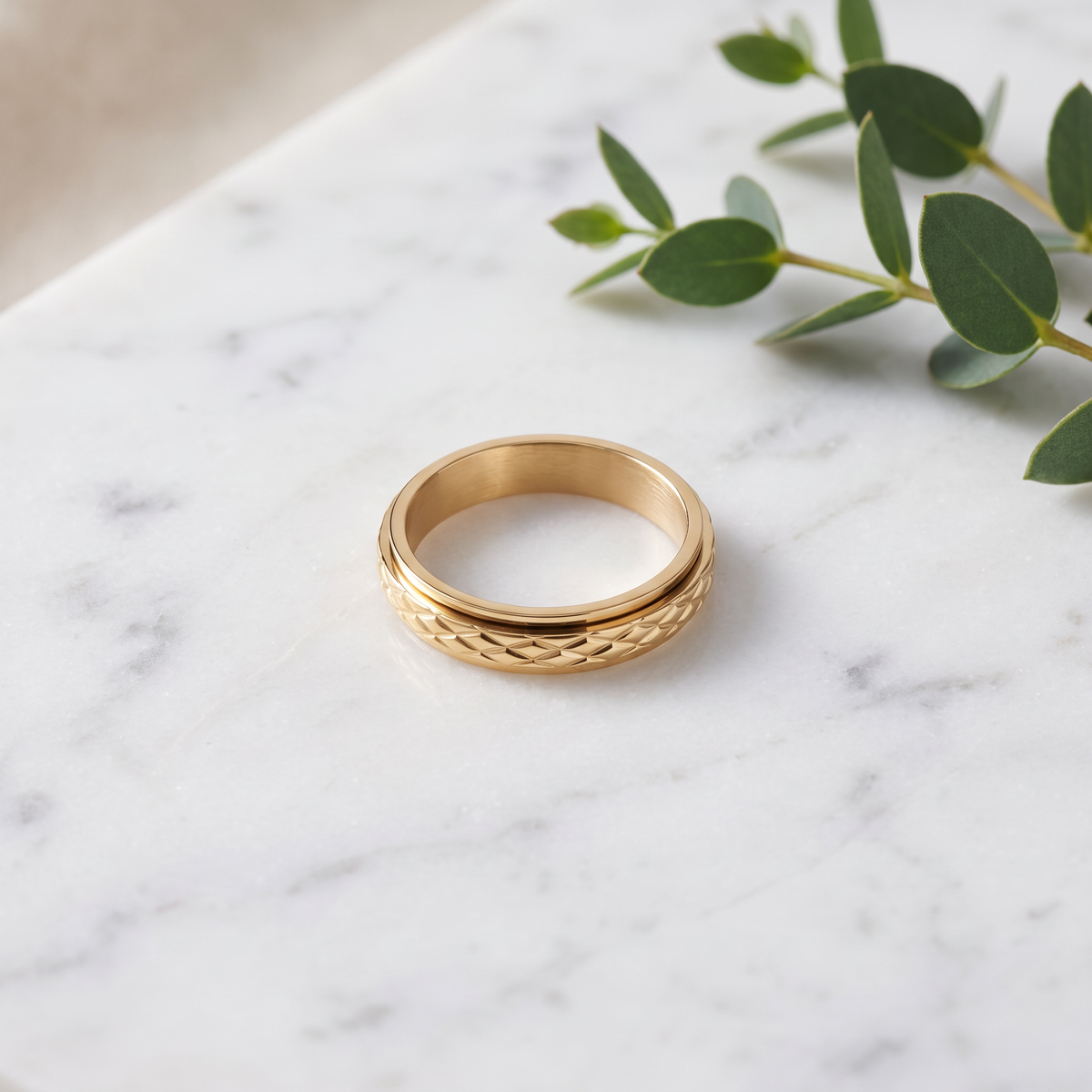 Gold Cross Pattern Spinning Ring on white marble with eucalyptus