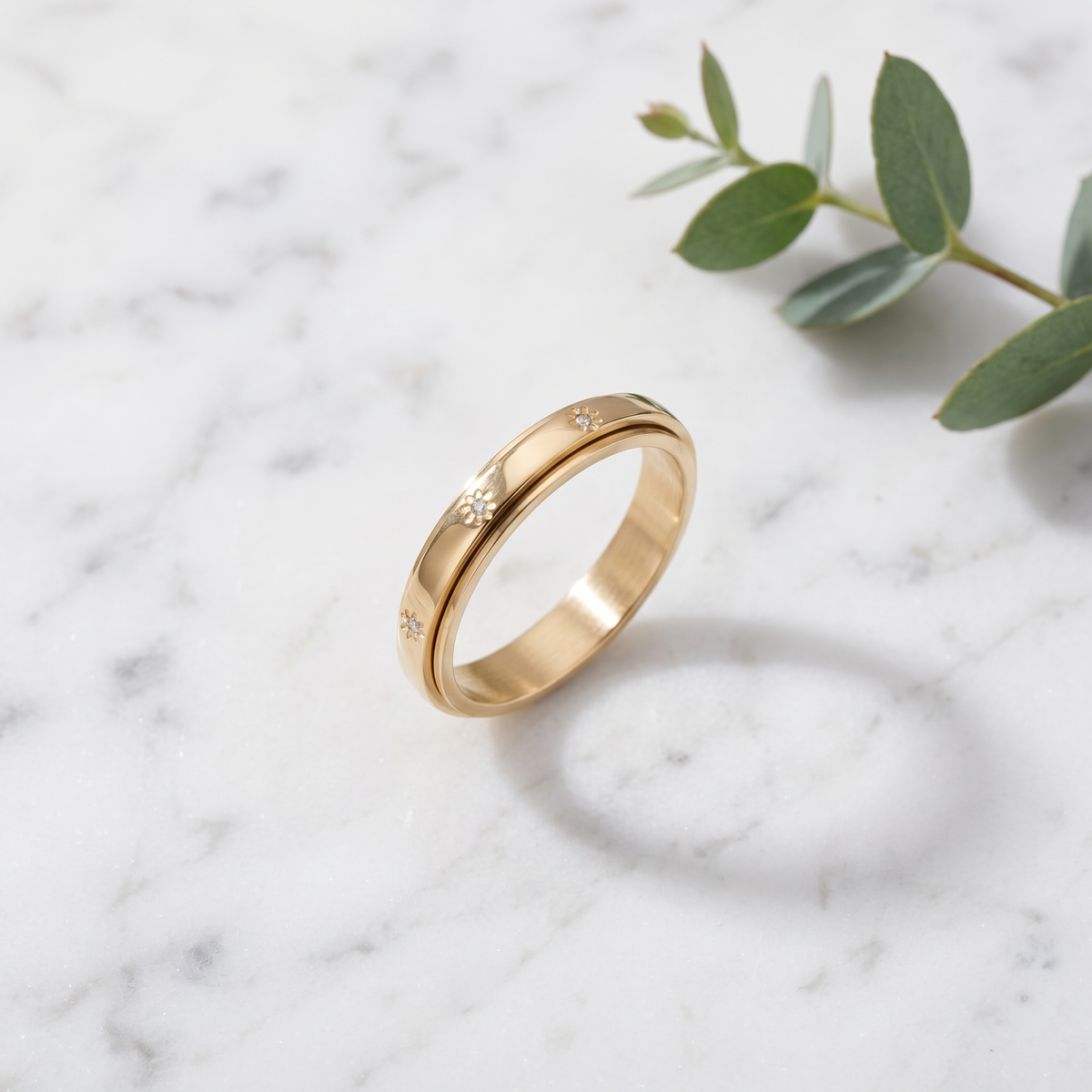 Gold Star Spinning Ring on white marble with eucalyptus