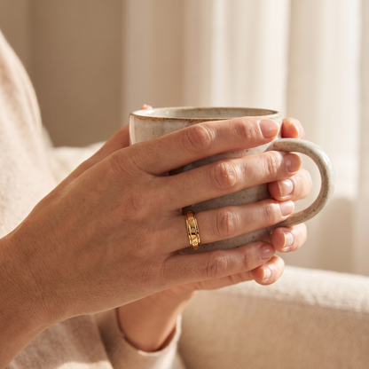 Hands holding a coffee mug, wearing the Gold Star Spinning Ring