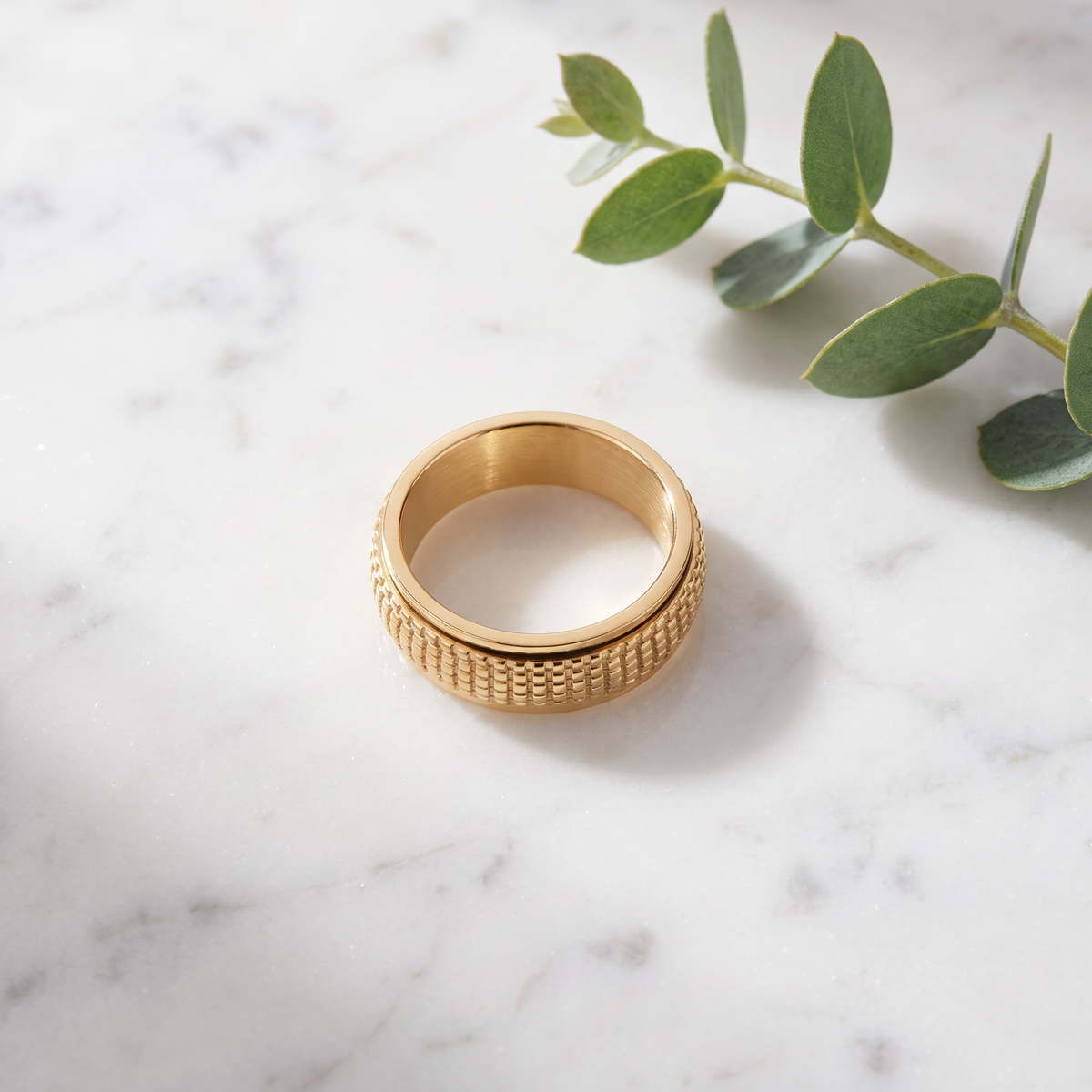 Gold Woven Spinning Ring on white marble with eucalyptus
