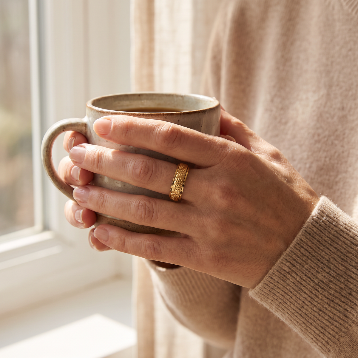 Hands holding a coffee mug, wearing the Gold Woven Spinning Ring