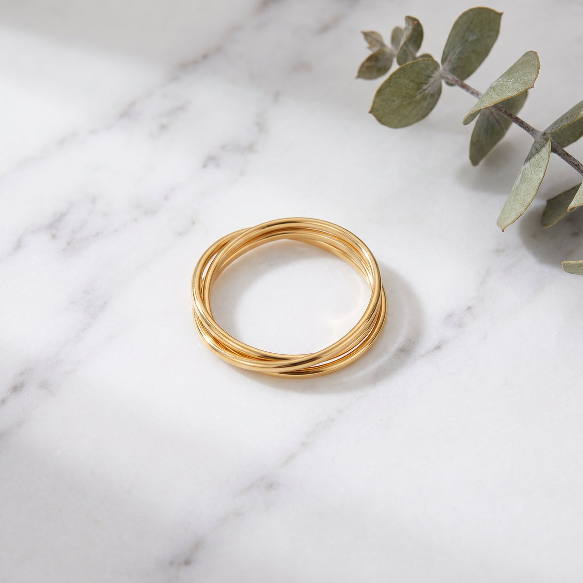 Gold braided rolling ring on white marble with eucalyptus