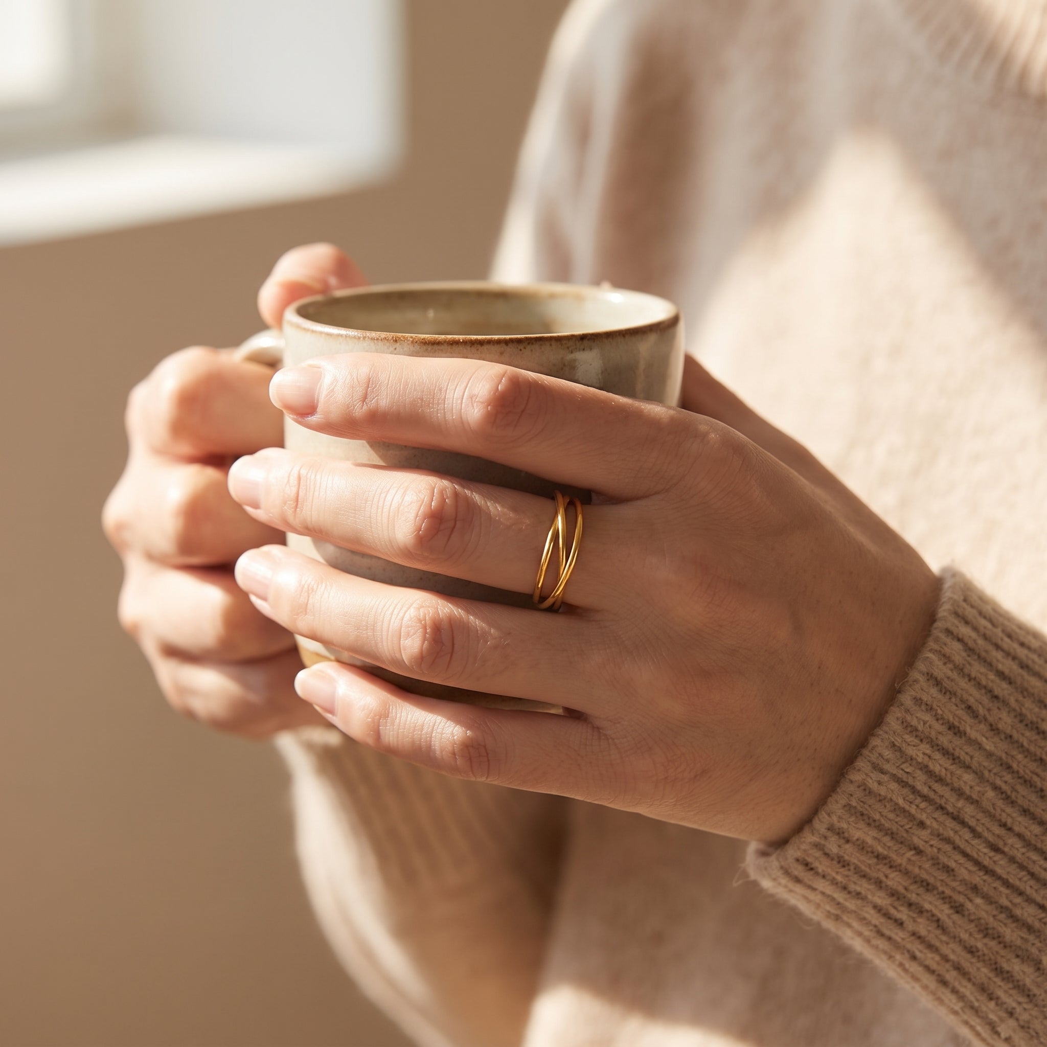 Hands holding a coffee mug, gold three-band rolling ring on the middle finger
