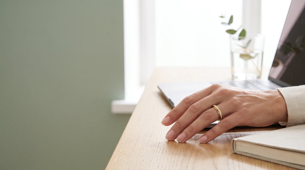 Hand resting on a desk next to a laptop, wearing the Loovina gold eternity spinning ring