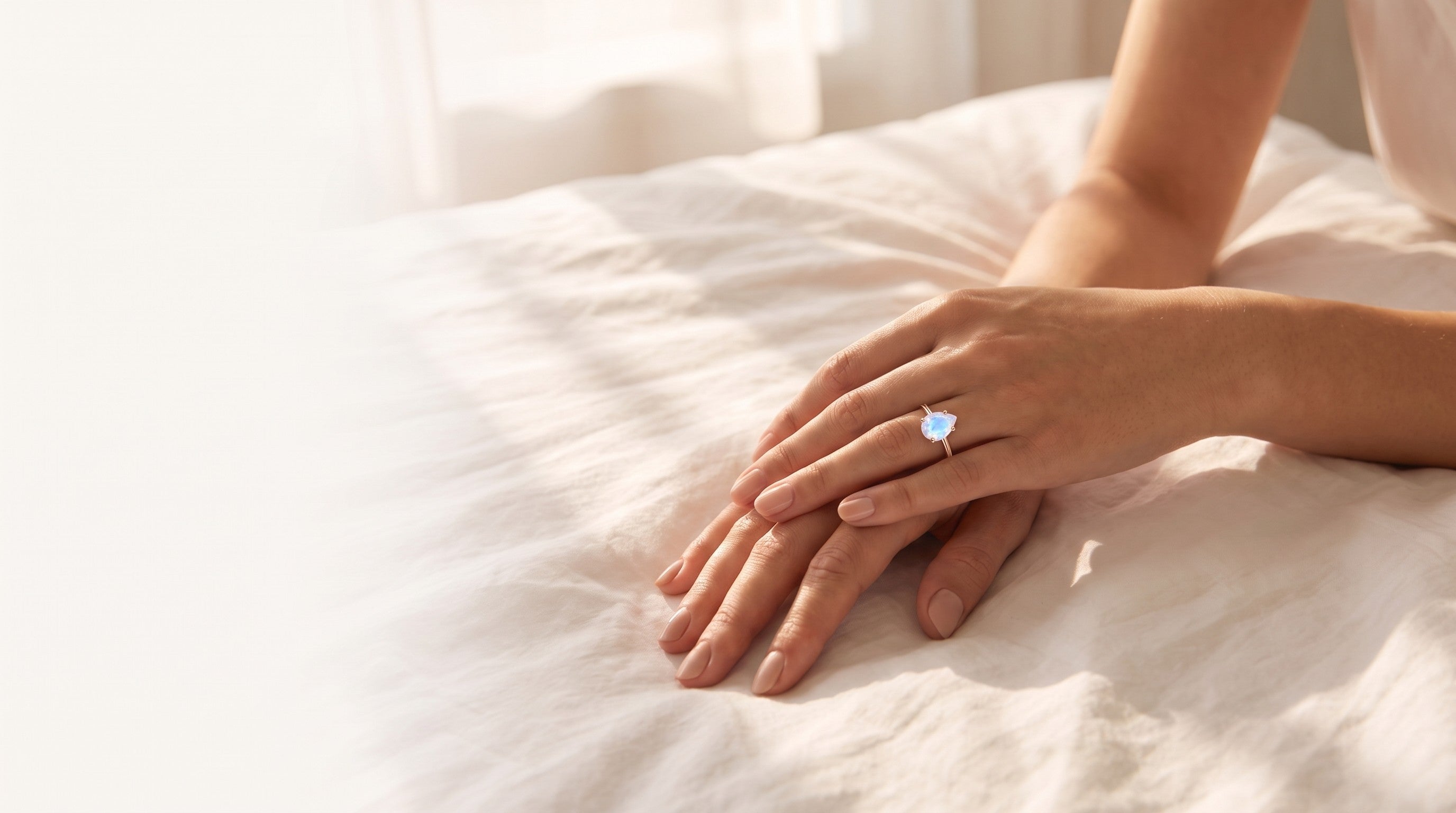 Hands resting on white linen, wearing a rose gold moonstone ring