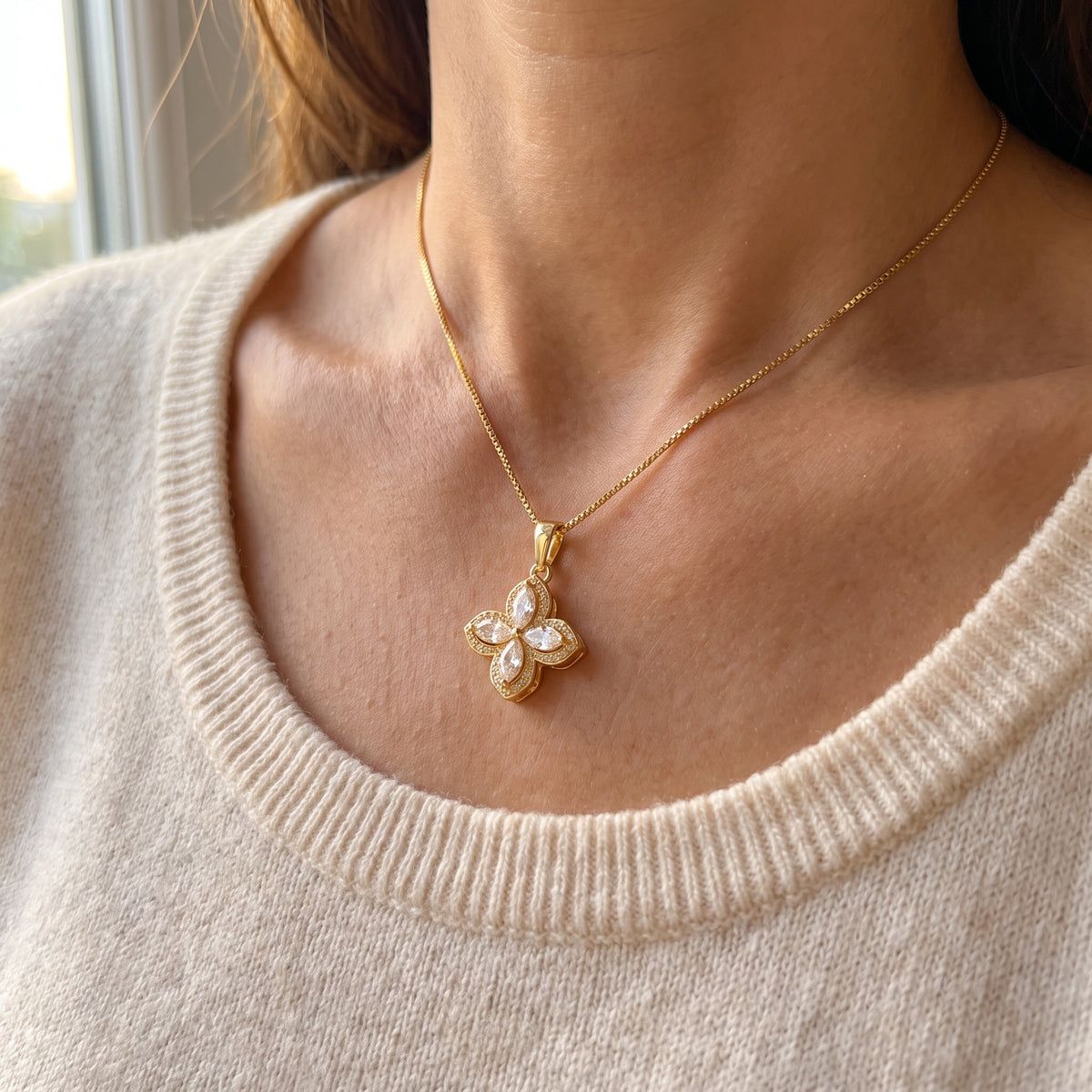Gold flower pendant worn with a cream knit sweater
