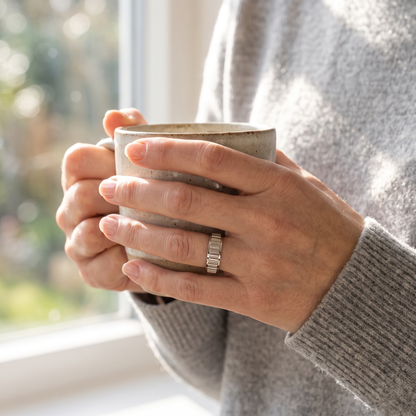 Hands holding a coffee mug, wearing the Silver Grooved Spinning Ring